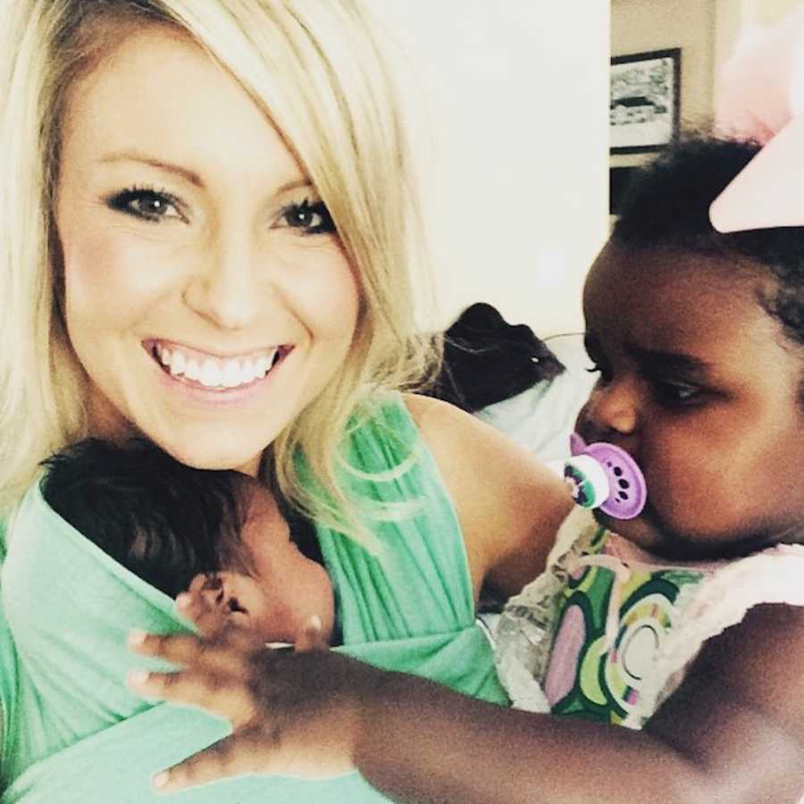 Woman smiles as she holds two adopted children in her arms