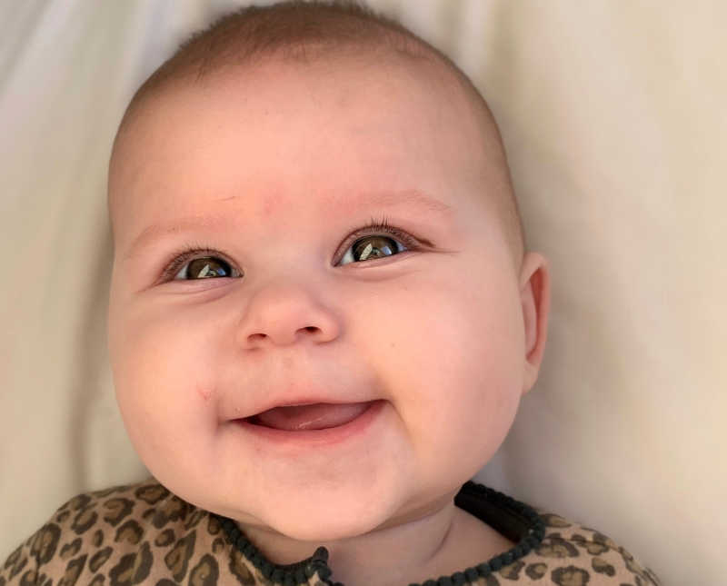 Baby girl lays on back smiling who has two mothers