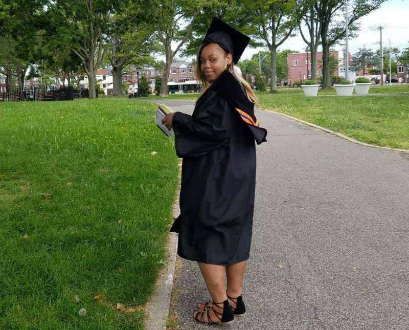 Young woman walks on sidewalk in black cap and gown