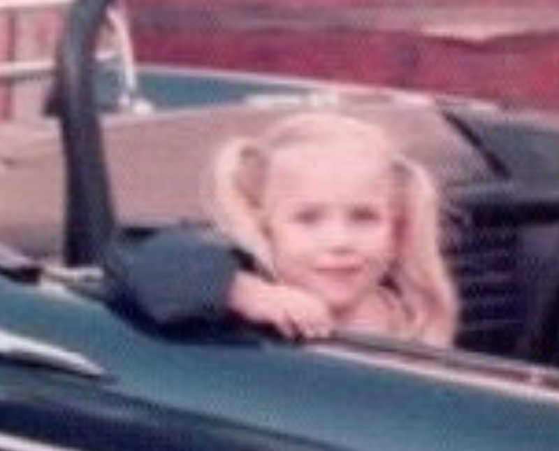 Little girl smiling as she sits in back seat of convertible