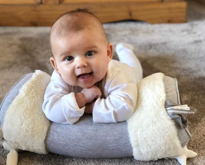 Baby girl with two mothers lay smiling on her stomach resting arms on pillow