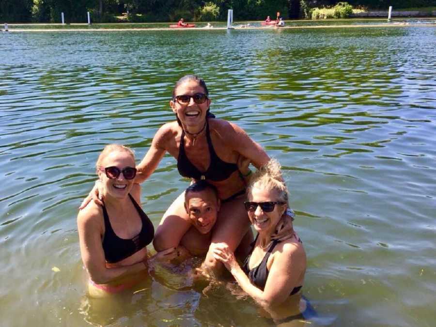 Woman who escaped abusive relationship sits on man's shoulders in water with two other women standing beside him
