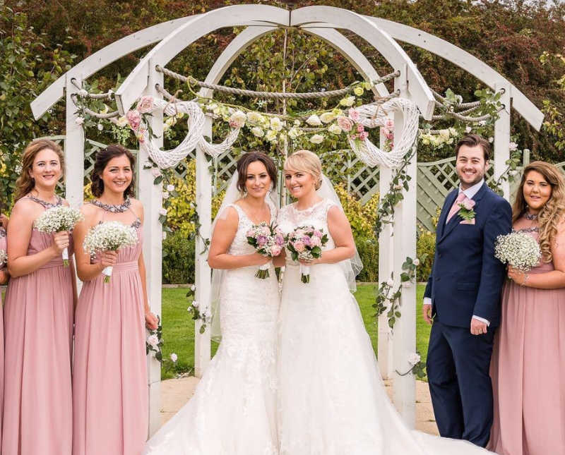 Brides stands at altar of outdoor wedding with their bridal parties on either side of them