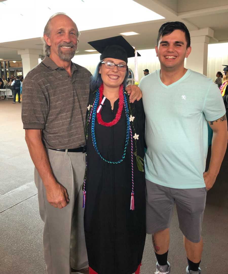 Woman who was kidnapped and abused stands in cap and gown beside father and fiancee