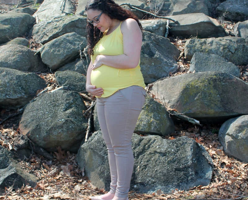 Pregnant woman stands holding her stomach outside near wall of rocks