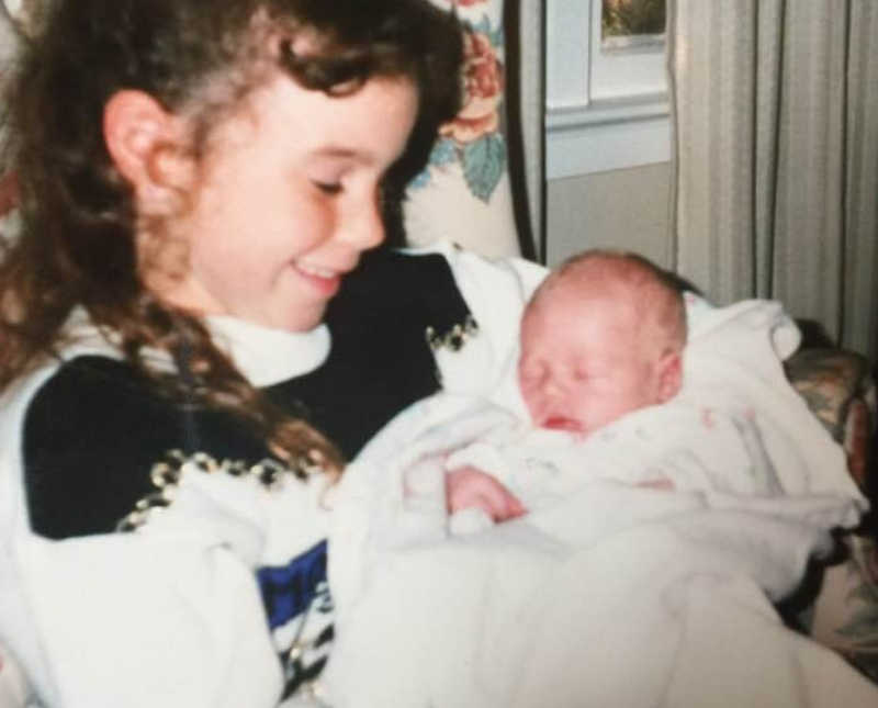 Young girl sits in chair holding sleeping baby boy who will grow up to have own family and pass at young age