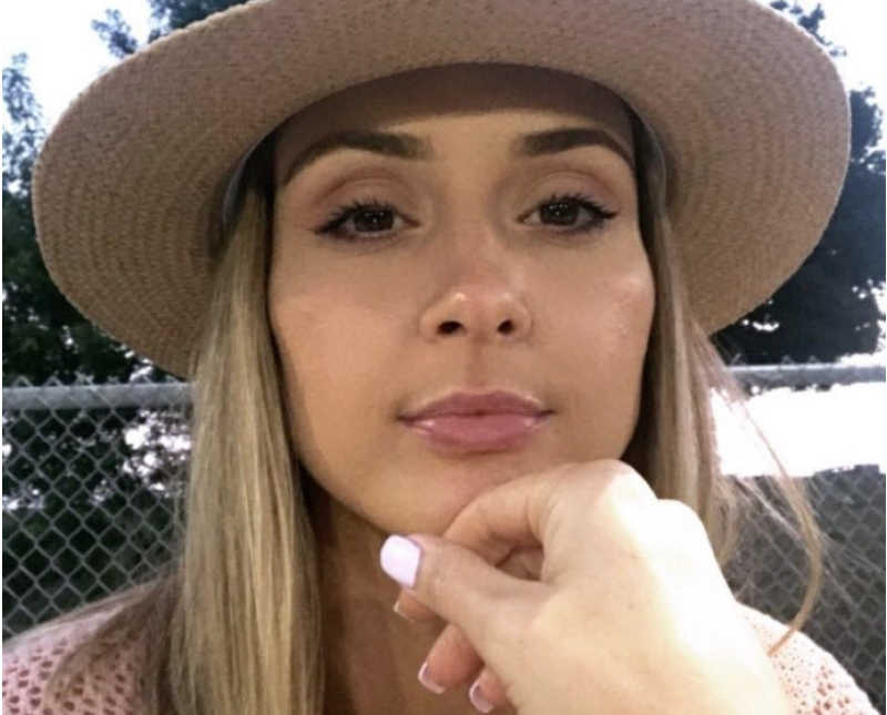 Woman who was domestically abused sits with straight face and hat on while someone touches her chin