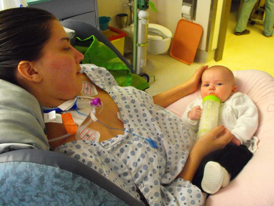 Mother with Guillain-Barre syndrome sits in hospital bottle feeding baby in her lap