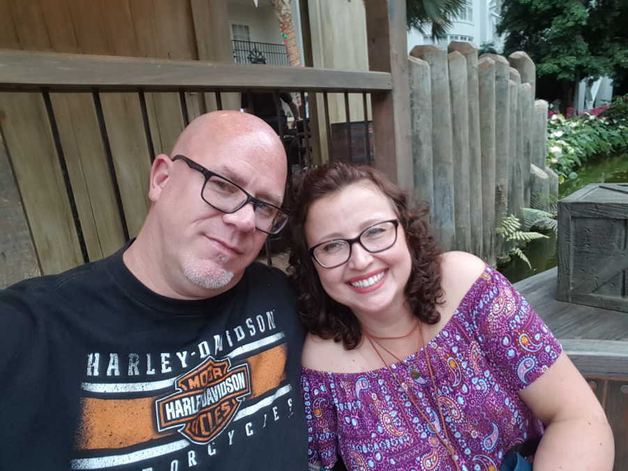 Man sits on bench outside smiling beside girlfriend in selfie