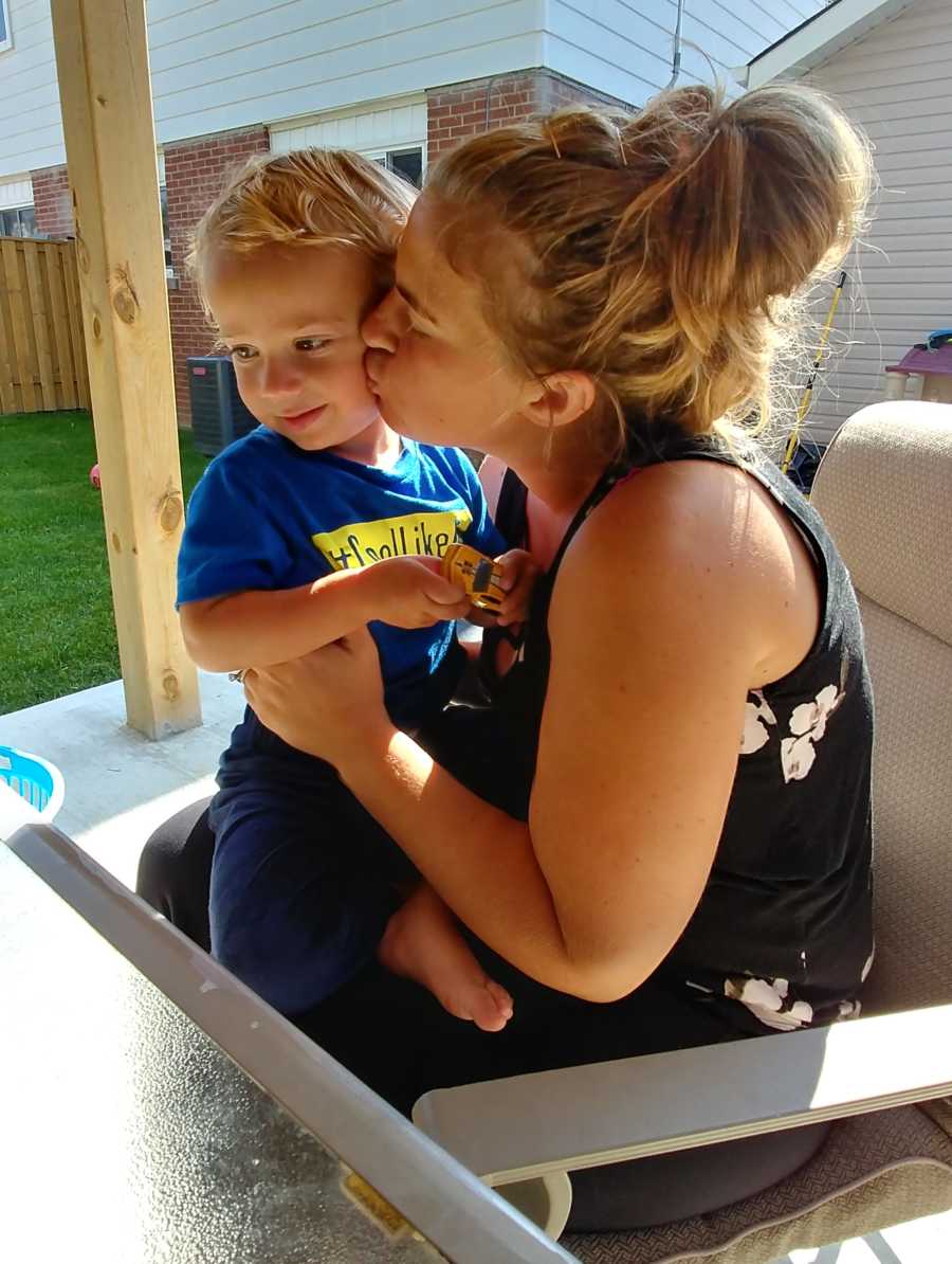 Woman who delivered empty placenta sits at table outside of home kissing her son on the cheek