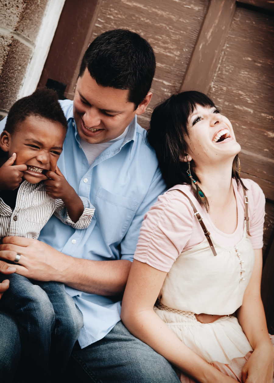 Husband and wife sit smiling as their adopted son makes silly face