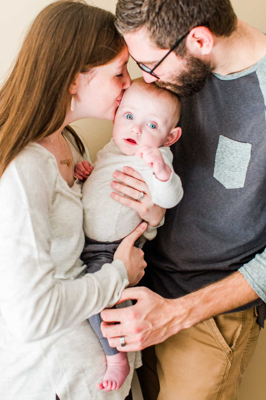 Mother and father kiss forehead of baby that they hold between them