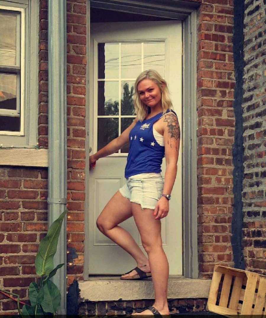 Young woman whose husband divorced her stands smiling outside as she opens door into home