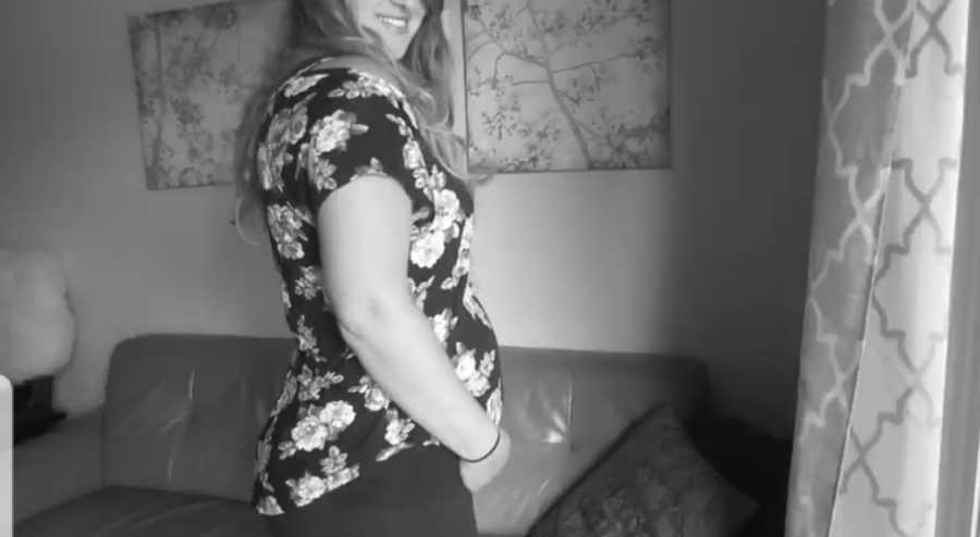 Pregnant woman smiles as she stands in home holding stomach