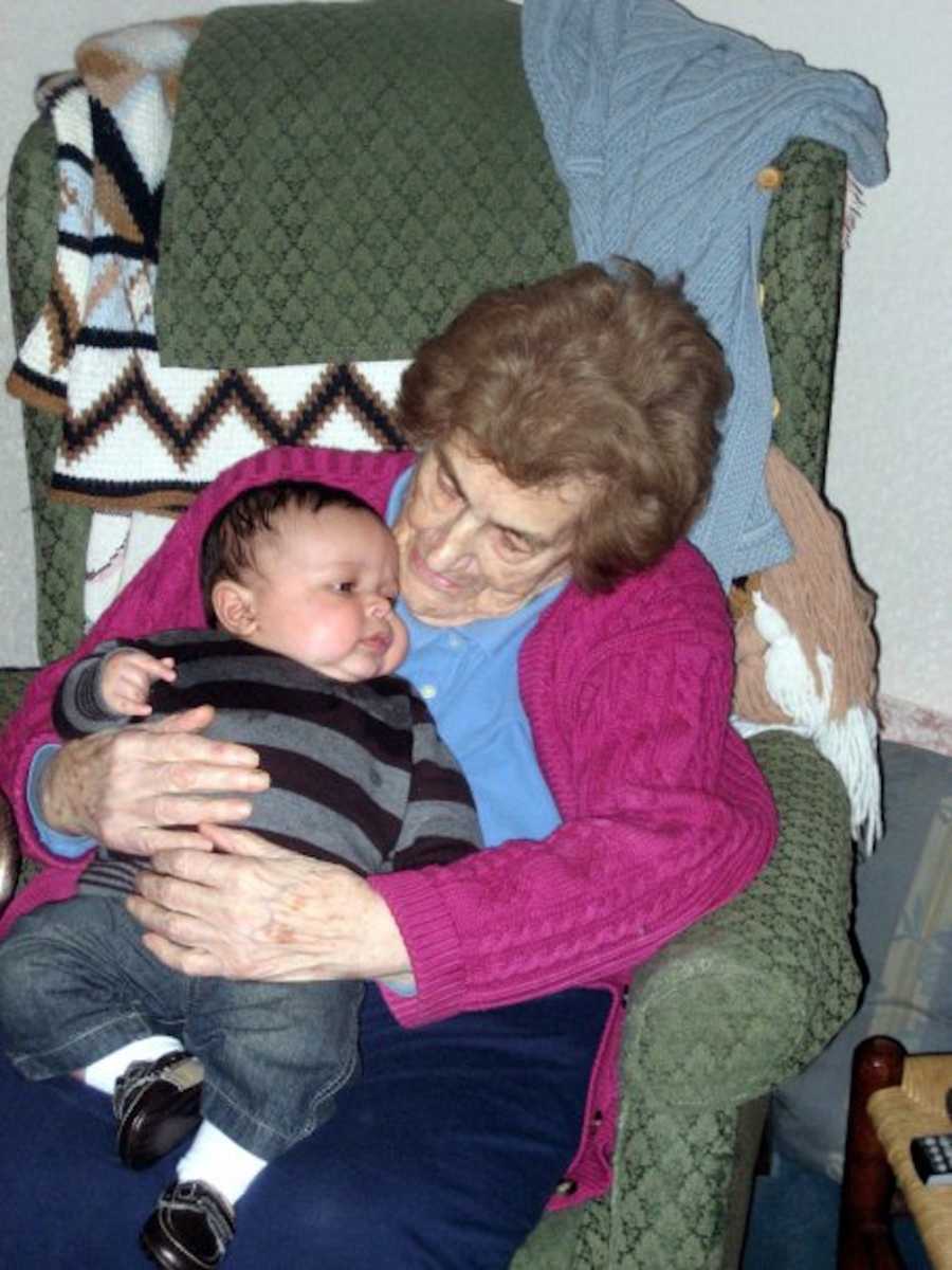 Elderly woman sits in chair in home with great grandchild in her lap