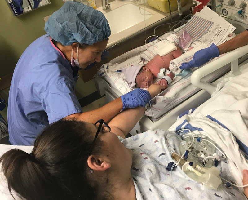 Nurse holds mother's arm who holds hand of newborn is paralyzed from ankle down