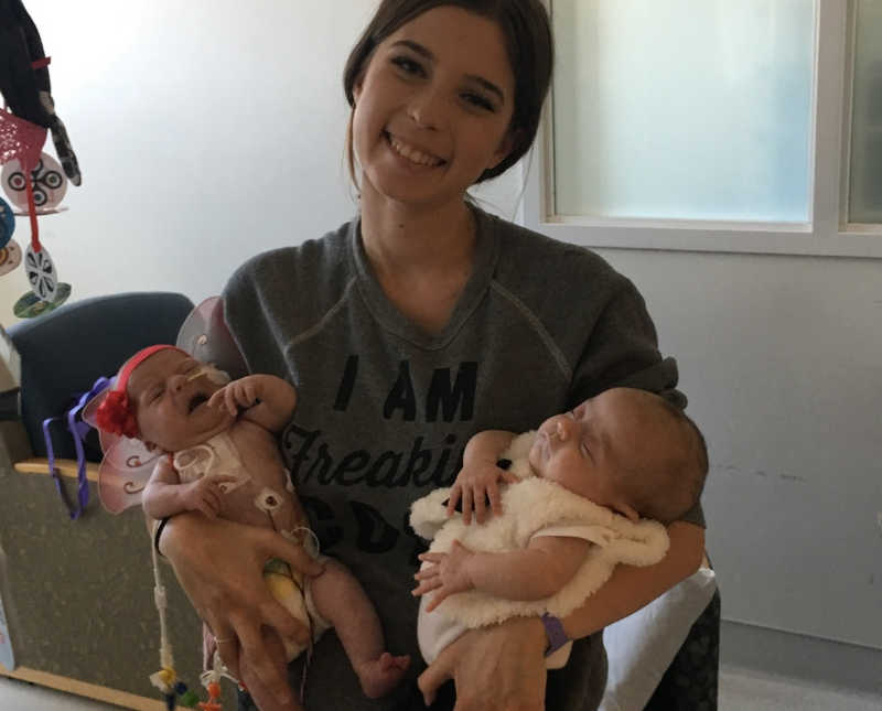 Mother stands smiling in hospital room holding newborn twins in her arms