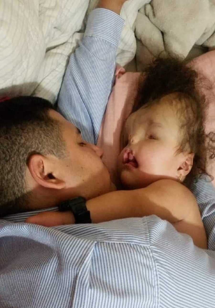 Father lays asleep beside daughter with severe birth defects