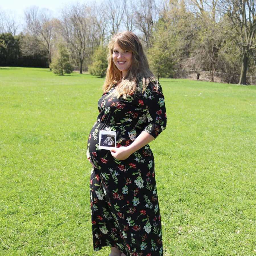 Pregnant woman stands outside holding ultrasound picture in front of her stomach
