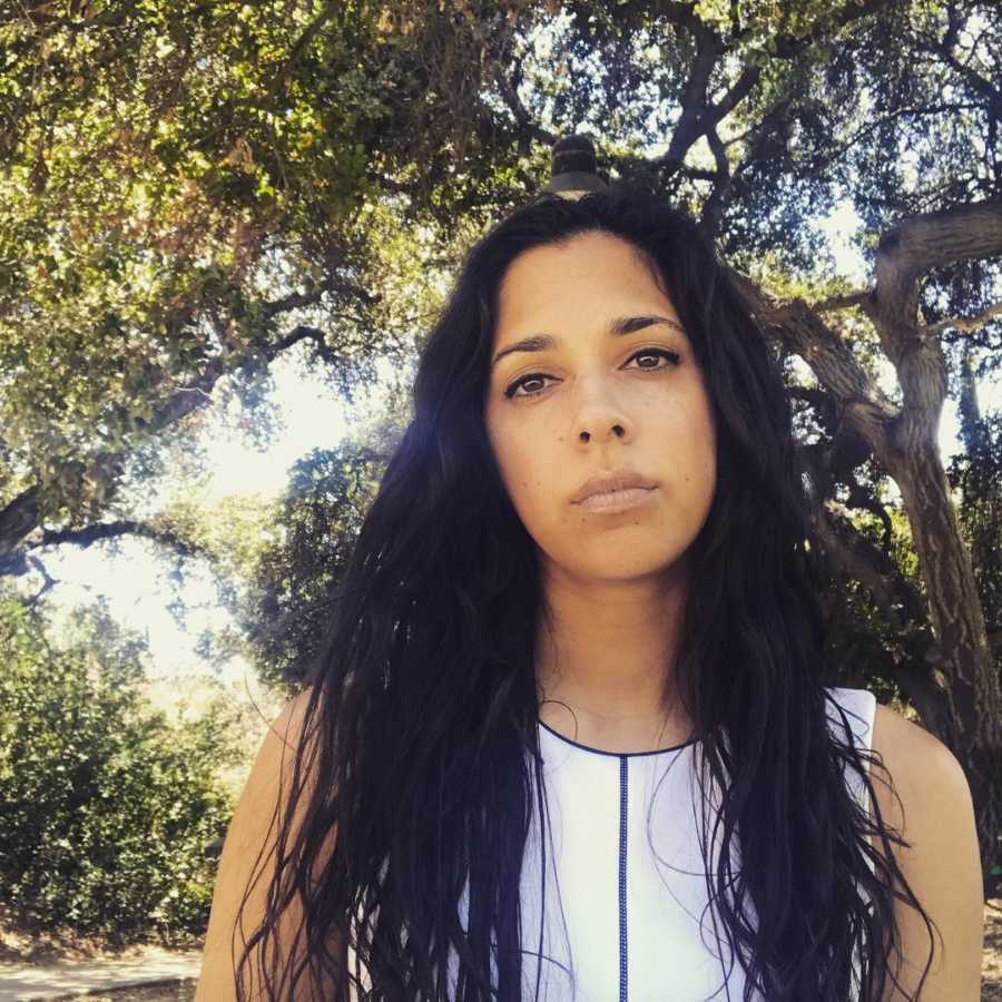 Woman who survived night club shooting stands with straight face outside under tree