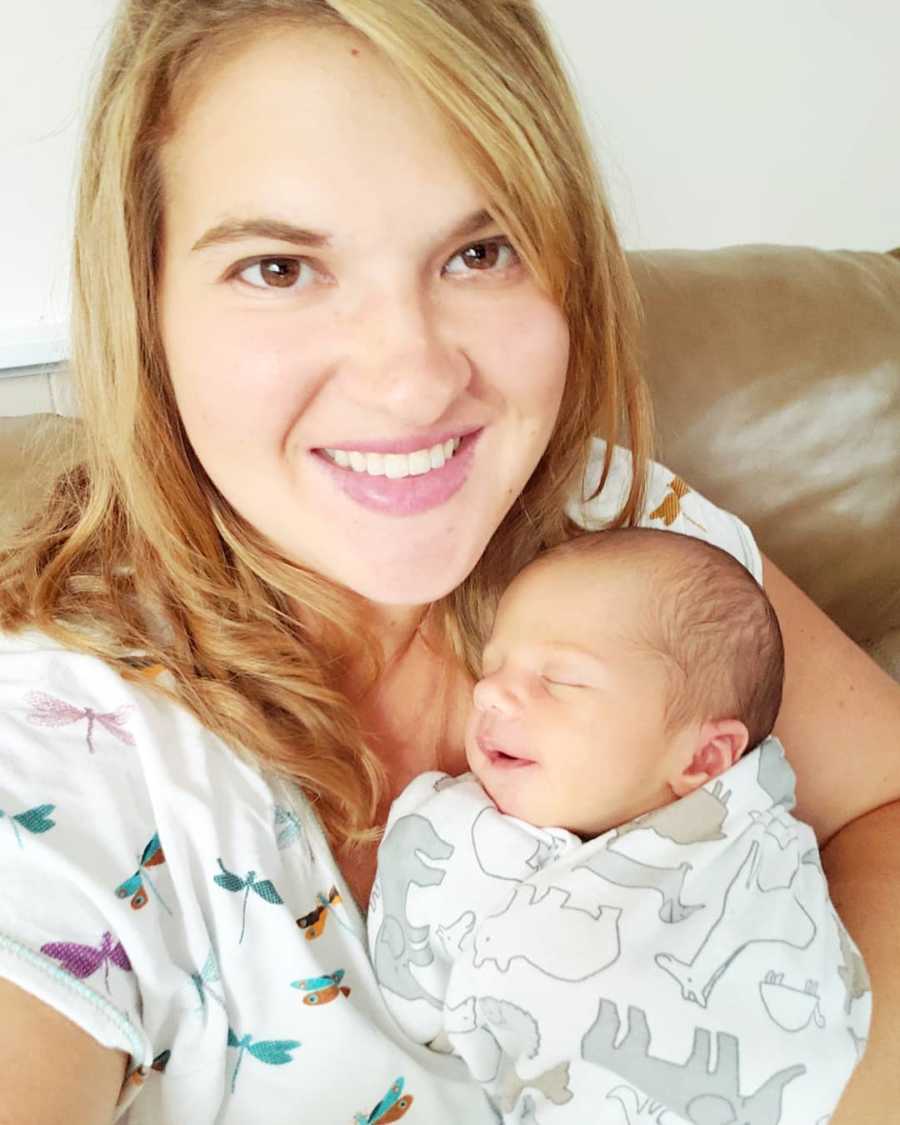Woman smiles as she sits holding newborn in her arm