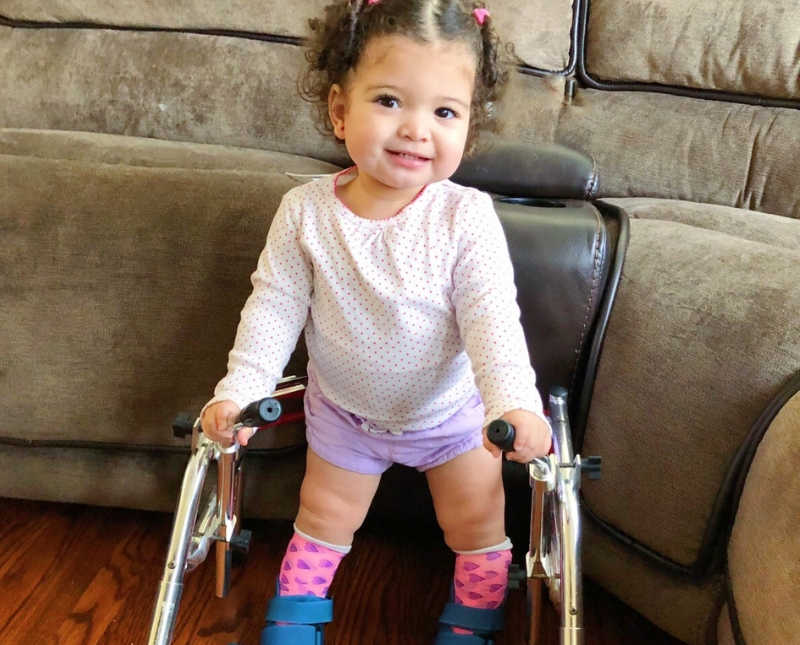 Little girl with Spina Bifida stands smiling with walker and casts on her legs