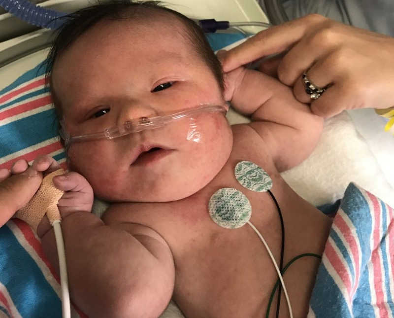 Newborn with down syndrome lays on back as he holds his mother and father's finger