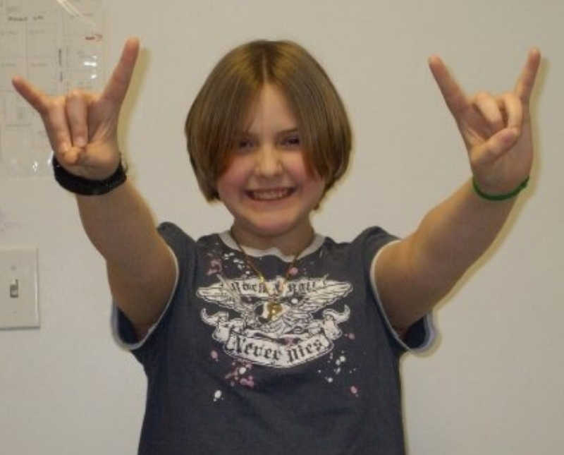 Young girl stands smiling holding her hands out with rock out sign