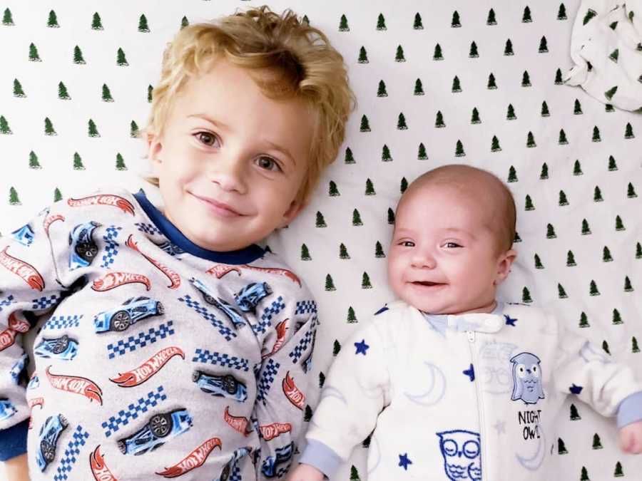 Little boy smiles as he lies on his back beside his baby brother