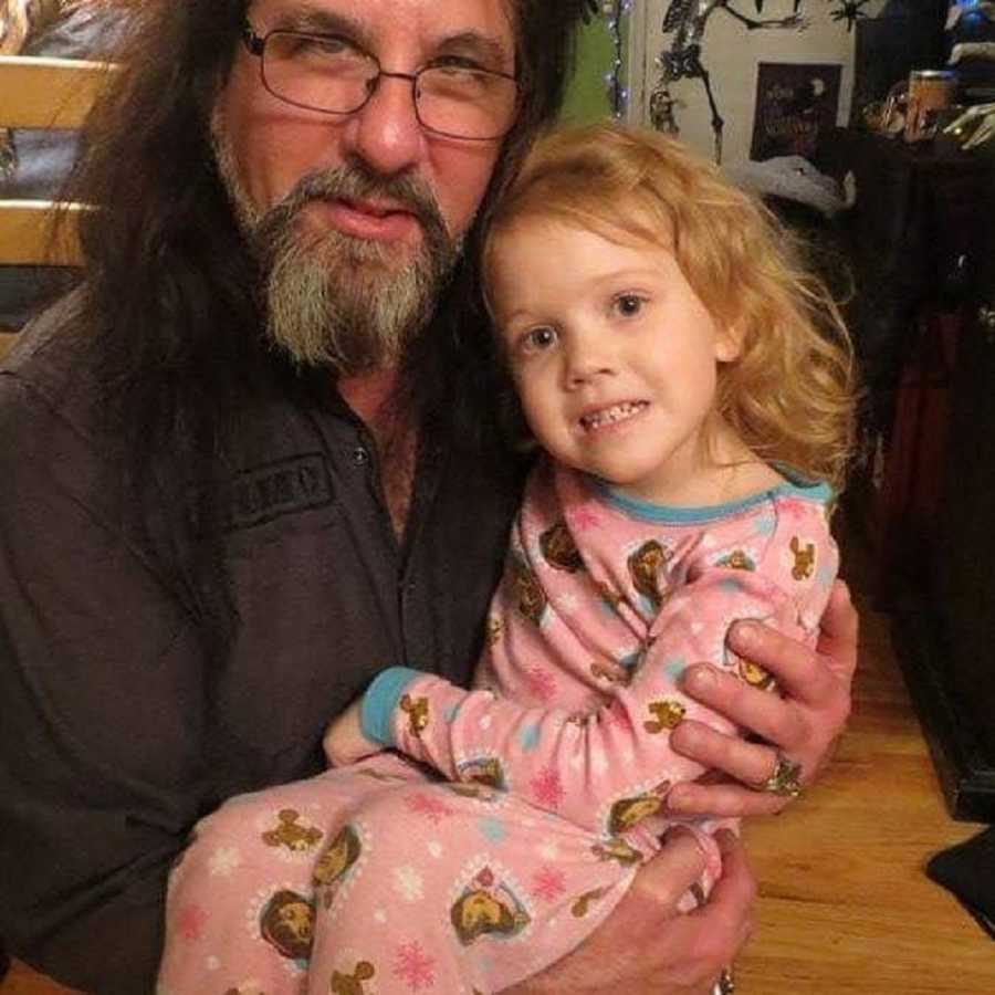 Father holds toddler daughter in his arms as she smiles