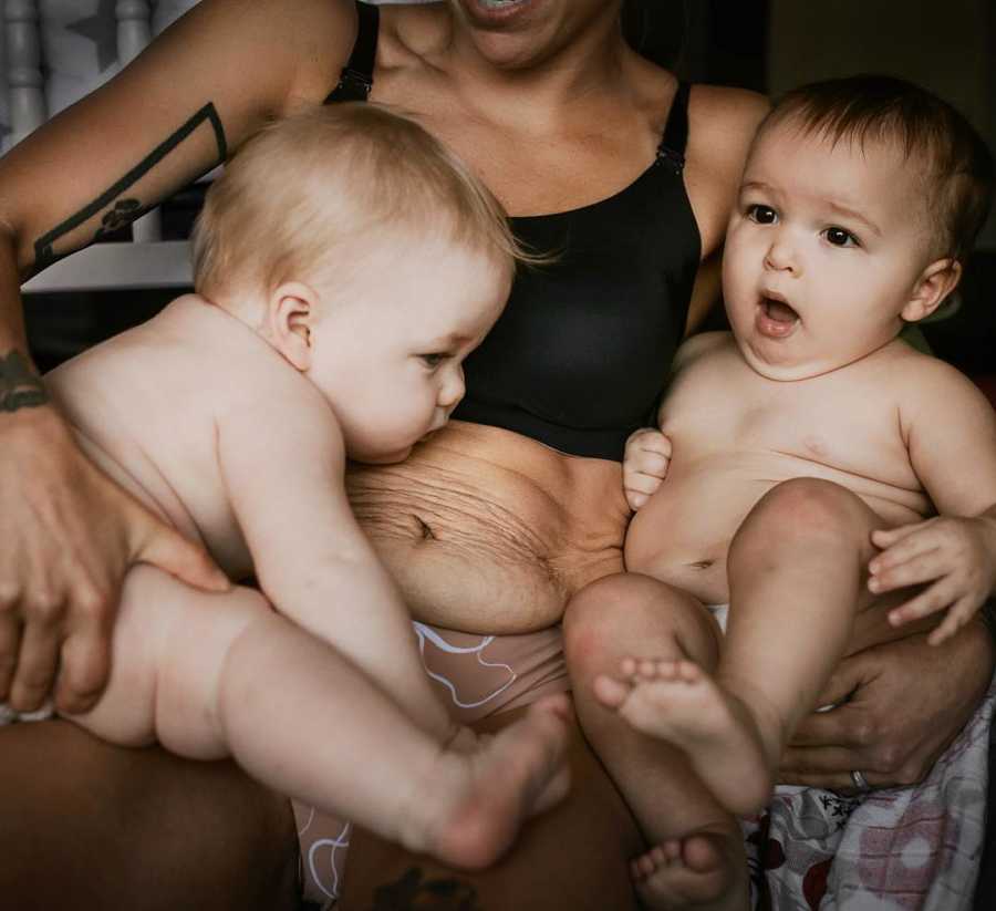 Mother sits in bra and underwear as she holds baby twins in her lap