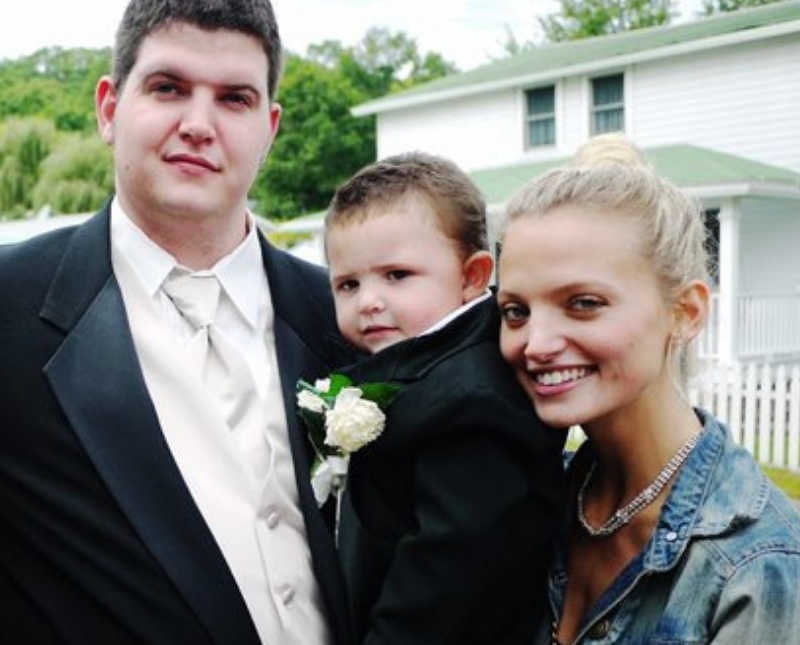 Drug addict stands in suit holding his son beside his wife