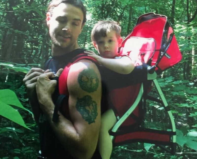 Man who has since passed stands in forest with son strapped to his back