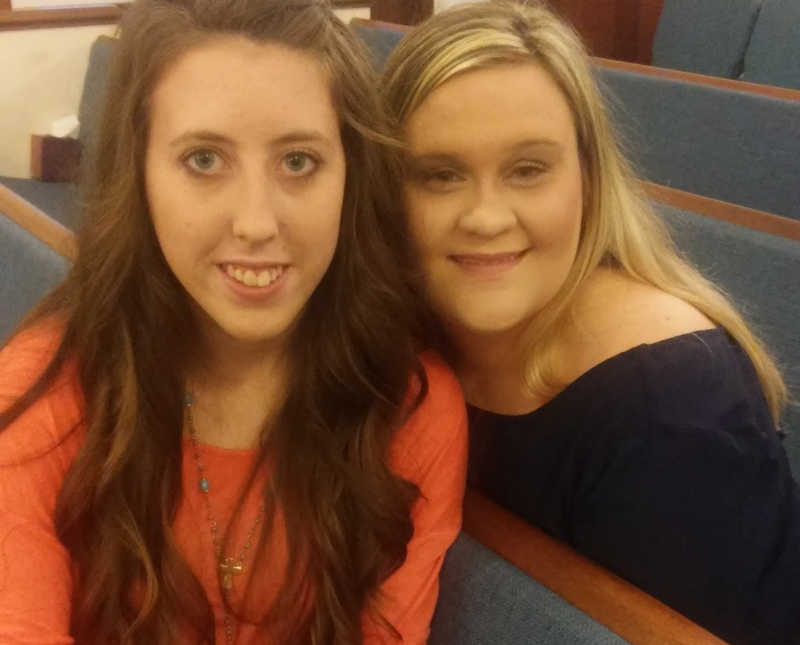 Woman who escaped abusive relationship sits in church pew smiling beside friend