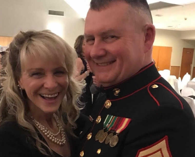 Woman with cancer smiles as she stands arm in arm with her husband who is in military