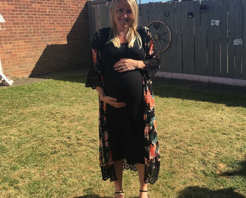 Pregnant woman stands in yard smiling as she holds her stomach