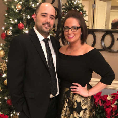 Husband and wife smile in home in front of Christmas tree