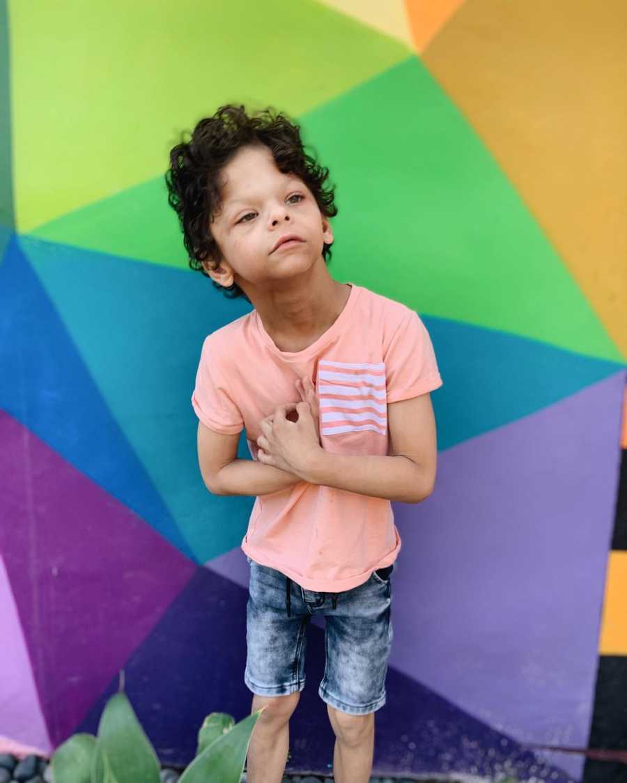 Little boy with Williams Syndrome stands in front of colorful wall