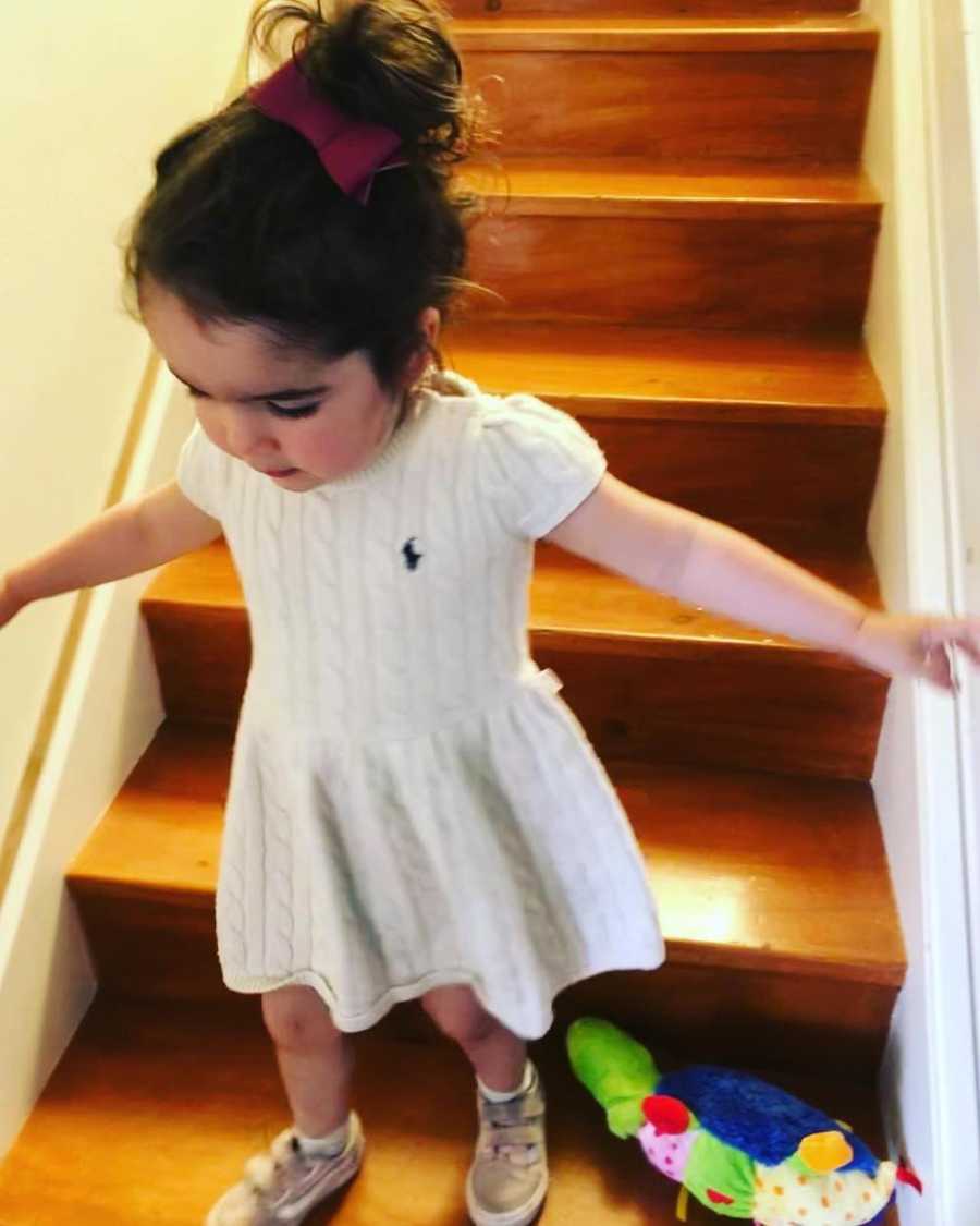 Little girl standing on staircase in home in white hand-me-down dress