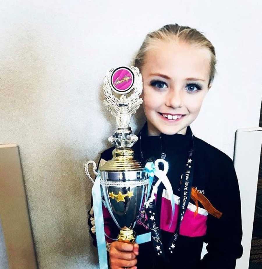 Little girl who does competitive dance smiles as she holds trophy