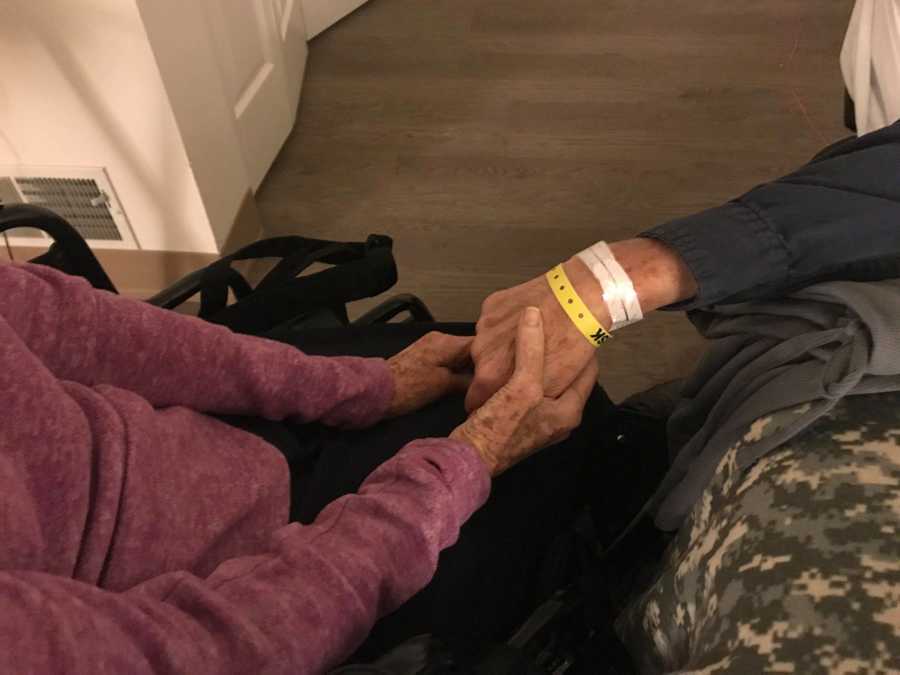 Close up of man laying in hospital bed holding hand's with his wife who has dementia