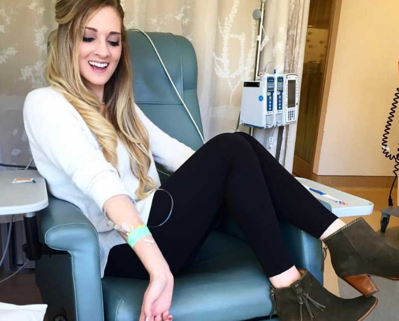 Woman with a precancerous colon sits in hospital chair smiling as she looks at IV in her arm