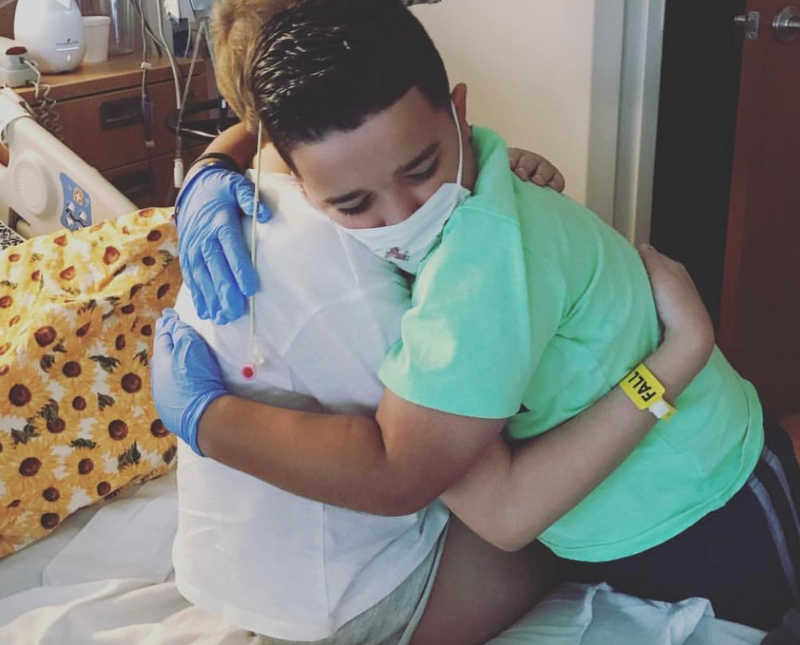 Young boy stands hugging sister with leukemia 