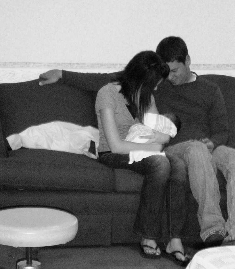 Husband and wife sit on couch in hospital as wife holds adopted newborn