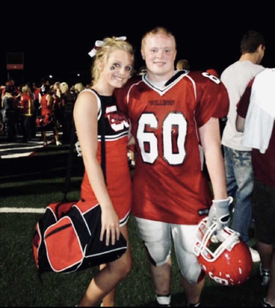 Teen who had a seizure from drinking energy drink stands on football field in uniform beside cheerleader