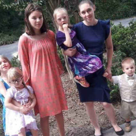 Mother stands outside holding daughter with down syndrome beside her four other kids