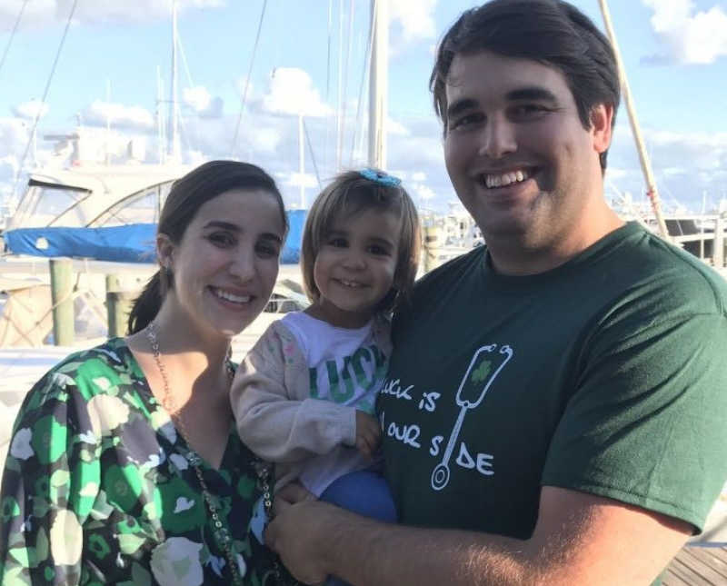 Husband holds his daughter as he stands beside his wife 