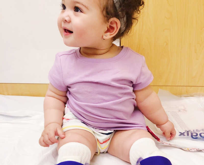 Baby girl with Spina Bifida sits in doctors office smiling with braces on her legs