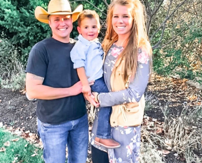 Husband and wife stand outside as they hold adopted little boy