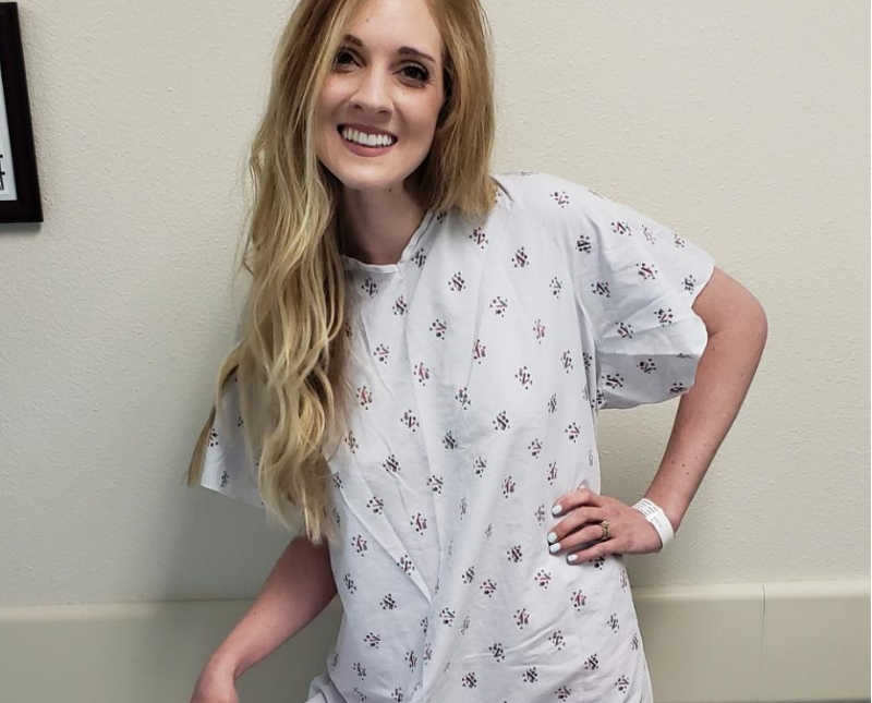 Woman with ileostomy bag for two years stands in hospital smiling in hospital gown